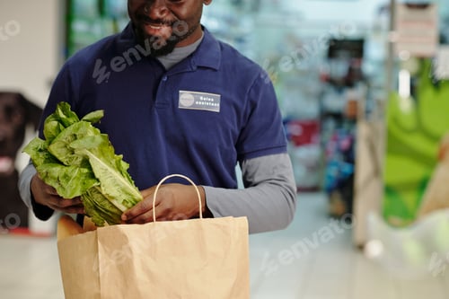 Preview: Close-up of young sales assistant putting vegetables into paperbag