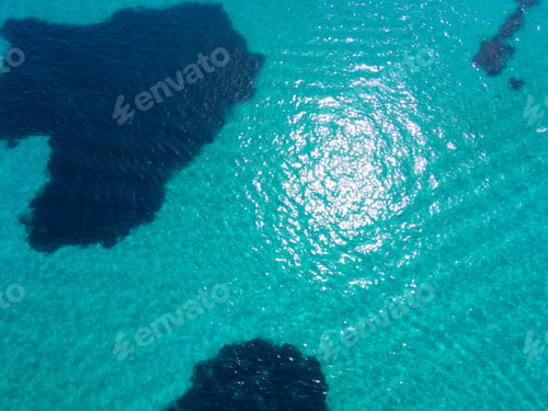 Preview: Aerial view of turquoise waters with sunlight reflecting off the surface and dark patches of coral