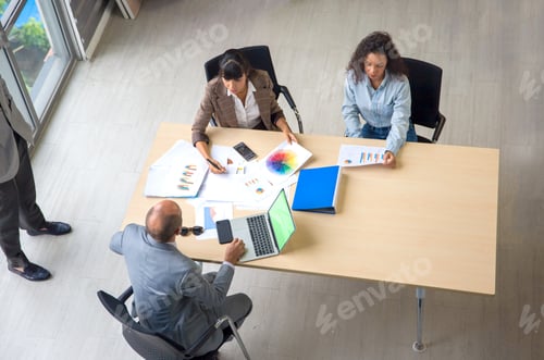 Preview: Young businessman giving some new ideas about project to his partners in conference room. above view