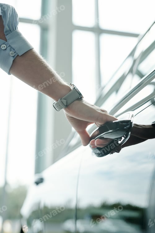 Preview: Hand of young sales manager of auto center holding by handle of new car