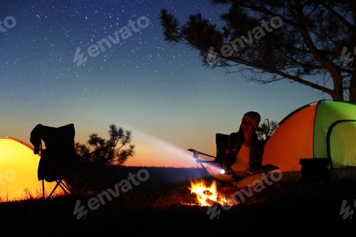 Preview: Woman with flashlight near bonfire at night. Camping season