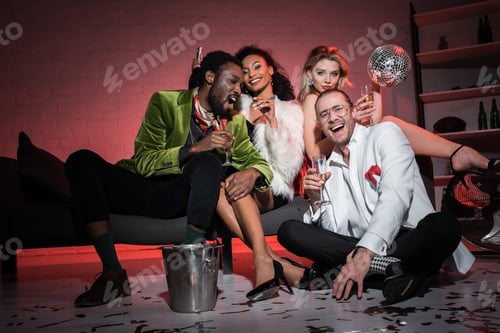 Preview: low angle view of attractive woman holding disco ball while sitting near multicultural friends