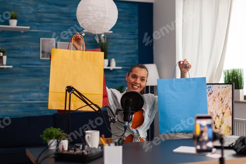 Preview: Woman content creator showing colorful paper bags for online giveaway