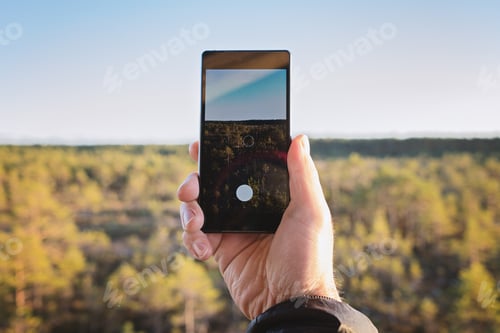 Preview: A man's hand holds a smartphone and makes a vertical photo of a beautiful fall landscape