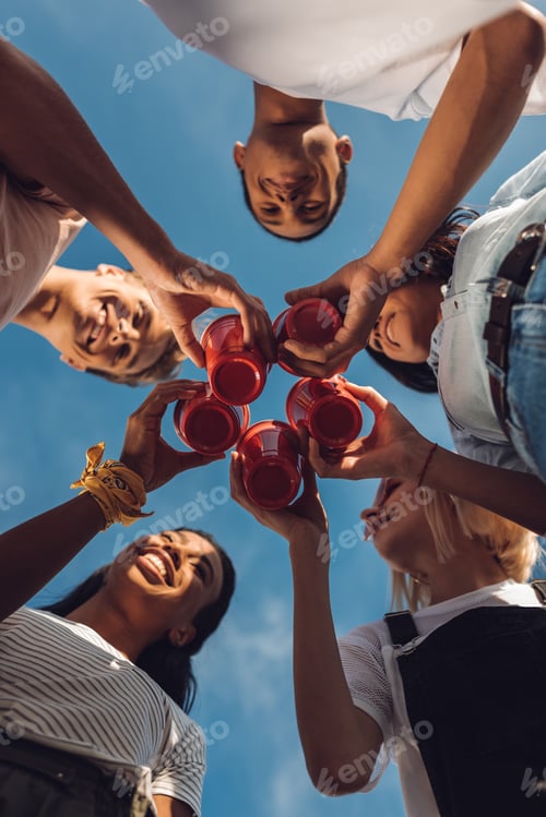 Preview: bottom view of friends clinking plastic glasses with alcohol outdoors
