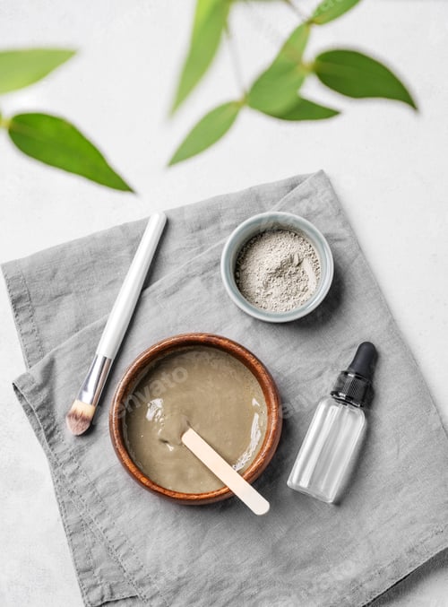 Vista previa: Flat lay of organic cosmetic with blue clay, serum, brush and branch on a light background.