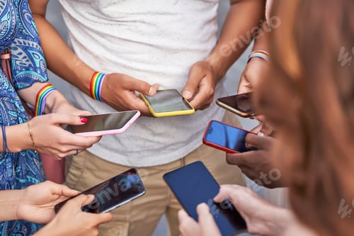 Preview: Group of people with LGBT flag wristbands using their mobile phones while standing together.