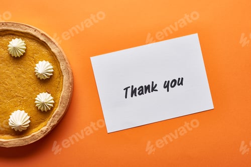 Preview: top view of pumpkin pie and thank you card on orange background