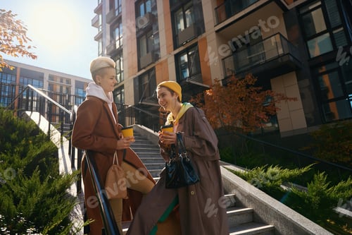 Preview: Laughing women, lgbt couple, communicate against backdrop of autumn cityscape