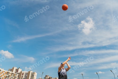 Preview: A basketball player launches a ball into the sky, framed by urban buildings and a clear blue sky.