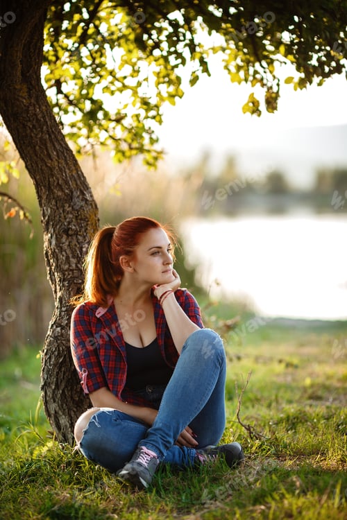 Preview: Attractive young woman enjoying her time outside in park with sunset in background.