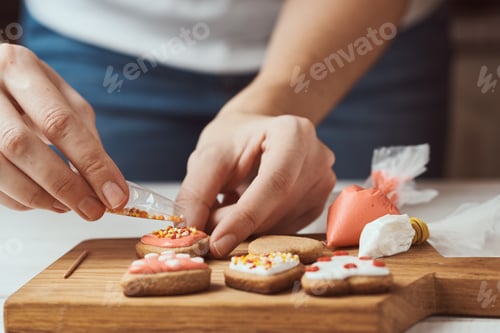 Preview: Decorating gingerbread cookies with icing. Woman hand decorate cookies in shape of heart, closeup