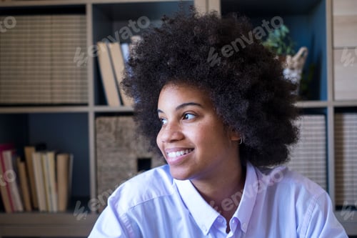 Preview: Attractive dark skinned young woman with curly Afro hairstyle looking out through window.