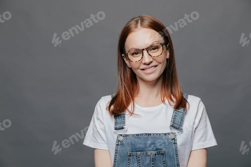 Preview: Isolated shot of positive pretty woman tilts head, has charming smile, wears glasses