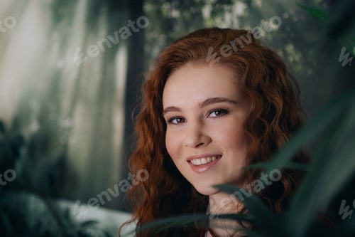Preview: Portrait of a beautiful young girl with red hair among the leaves of a plant