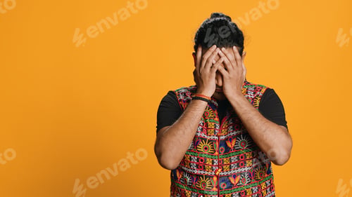 Preview: Man covering face with palms in disbelief, feeling upset, studio background