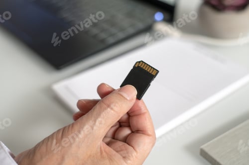 Preview: Man holding an SD card to insert in a laptop.