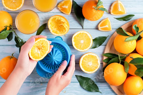 Preview: Woman squeezing fresh orange juice on blue wooden table