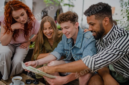 Preview: Group of happy young people sitting in outdoors cafe on town trip, using map