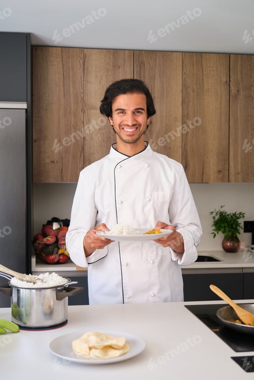 Preview: Indian chef holding plate of food smiling in kitchen