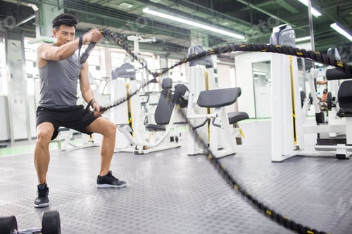 Preview: Young man exercising with battling rope at gym