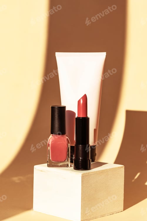 Preview: Cosmetic cream tube, pink nail polish and lipstick on wooden stand. Strong shadows on neutral
