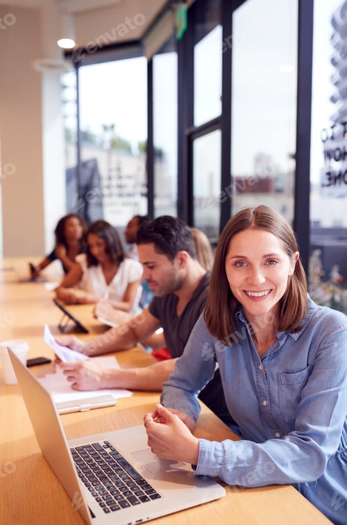 Preview: Portrait Of Businesswoman Working At Desk In Shared Open Plan Office Workspace
