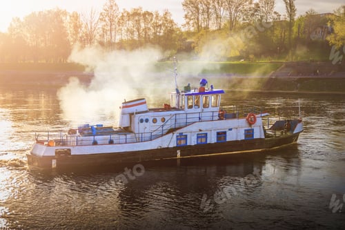 Preview: a small steamer ship on wide river in the rays of the setting sun