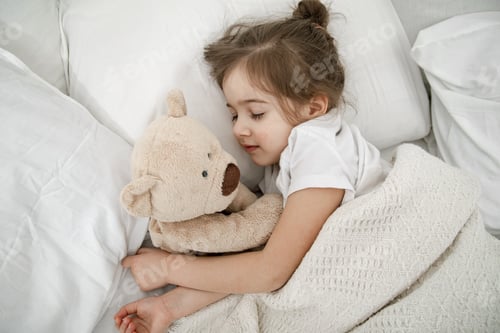 Preview: A cute little girl is sleeping in a bed with a Teddy bear toy .