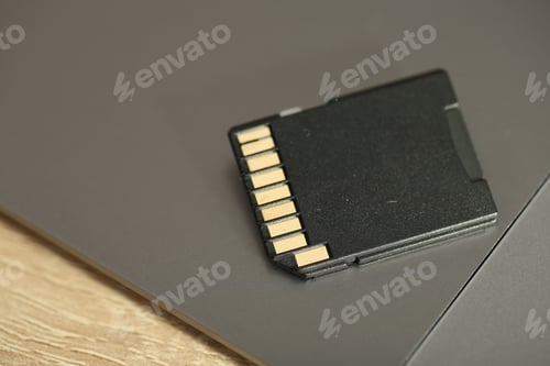 Preview: SD memory card and laptop on wooden table, closeup