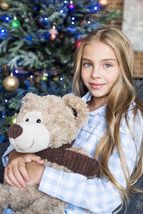 Preview: beautiful child holding teddy bear and smiling at camera at christmas time