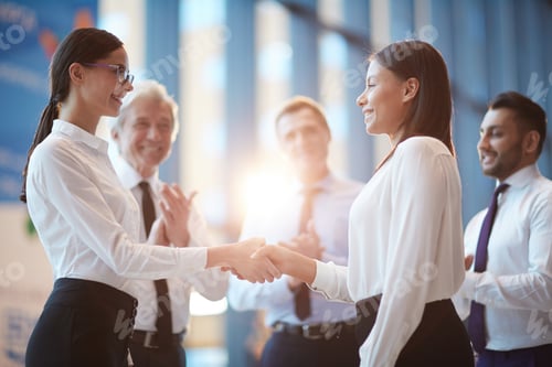 Businesswomen Shaking Hands While Coworkers Applaud
