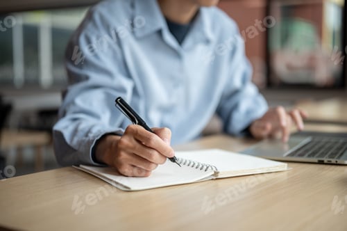 Preview: Hands holding fountain pen writing in notebook and typing on laptop while sits at wood table in cafe