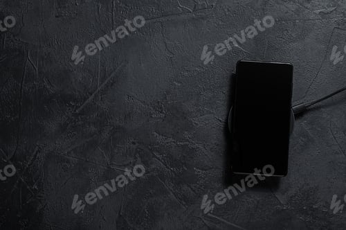 Preview: wireless charging pad for mobile phone. Black background. Top view. Space for text