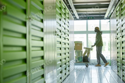 Preview: Black Man Transporting Boxes on Cart into Self Storage Unit at Warehouse while Moving out