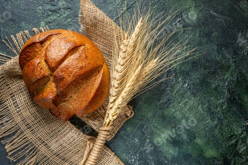 Preview: Top view of a loaf of dietary black bread and spikes on brown towel on dark colors background