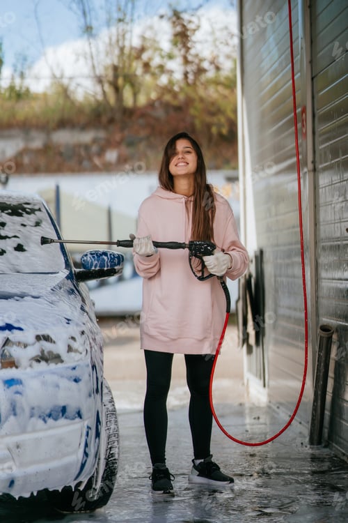 Preview: Brunette from a high-pressure hose applies a cleaner on the car