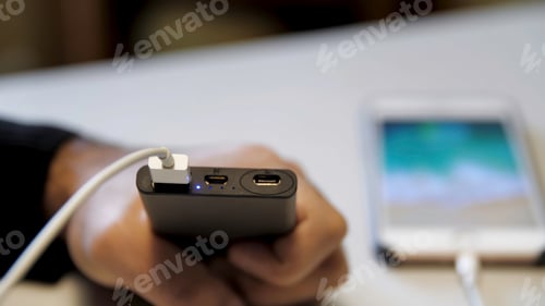 Preview: Black power bank and smartphone on a white table. Media. Close up of male hand inserting usb cable