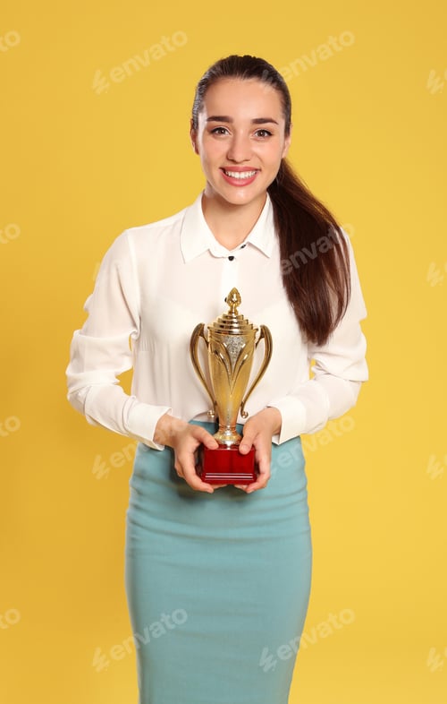 Preview: Portrait of happy young businesswoman with gold trophy cup on yellow background