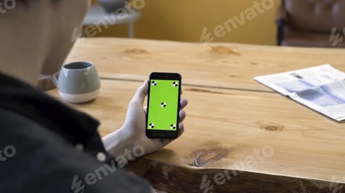 Preview: View over the shoulder of a businessman using the hand held cellphone with green screen touchpad on