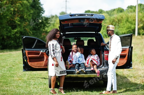 Preview: African family in traditional clothes stand against their car, kids sit on trunk.