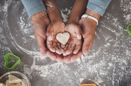 Preview: Shot of an unrecognizable girl and her mom holding a heart shaped cookie in the kitchen at home