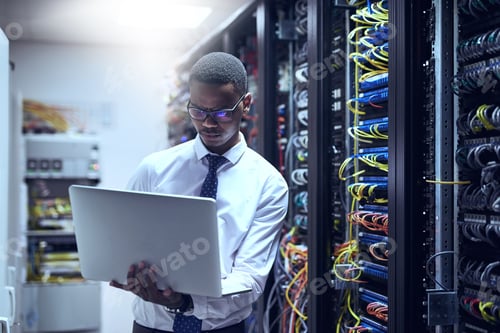 Preview: Cropped shot of a IT technician working on his laptop while standing inside of a server room