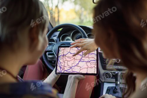 Preview: Happy young two women driver tourist travelers with digital tablet USA map at rental car vehicle.