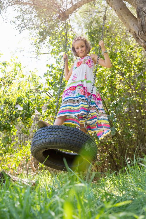 Preview: Portrait of girl standing swinging on tree swing in garden