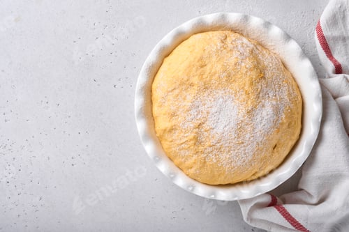 Preview: Raw yeast dough with pumpkin in white bowl covered with towel on the floured kitchen table, recipe i