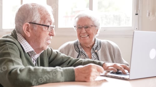 Preview: Happy senior couple chatting online using laptop at nursing home