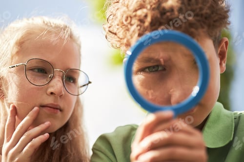Preview: Caucasian Girl and Caucasian Boy Examining Object Outdoors Using Magnifying Glass