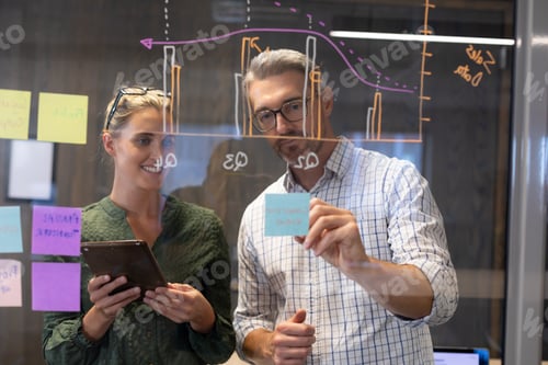 Preview: Caucasian business colleagues planning strategy together seen through glass wall in workplace
