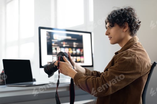 Preview: Positive male photographer holding camera while working with photos, looking through taken pictures